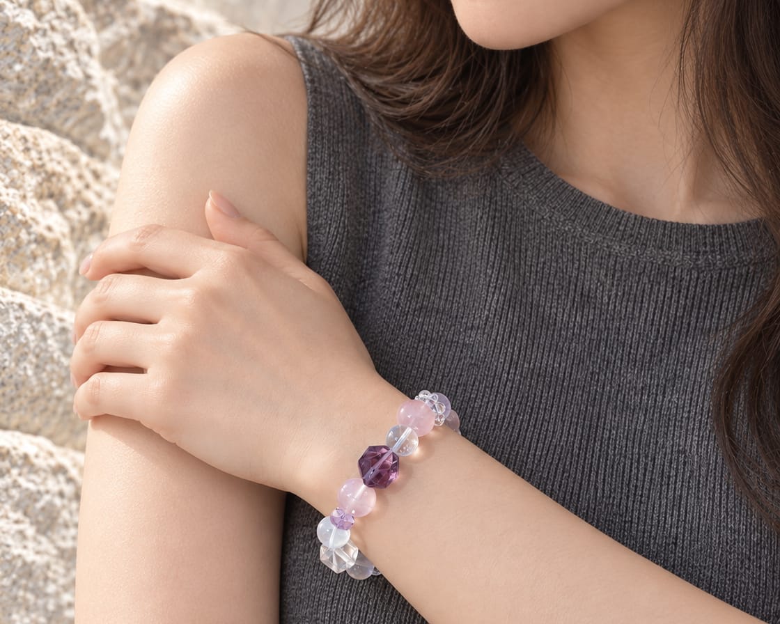 Woman wearing a rose, clear and violet gemstone bracelet beside pale mineral rock